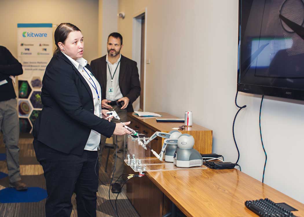 Kitware employee works with robotic arms while looking at tv screen.